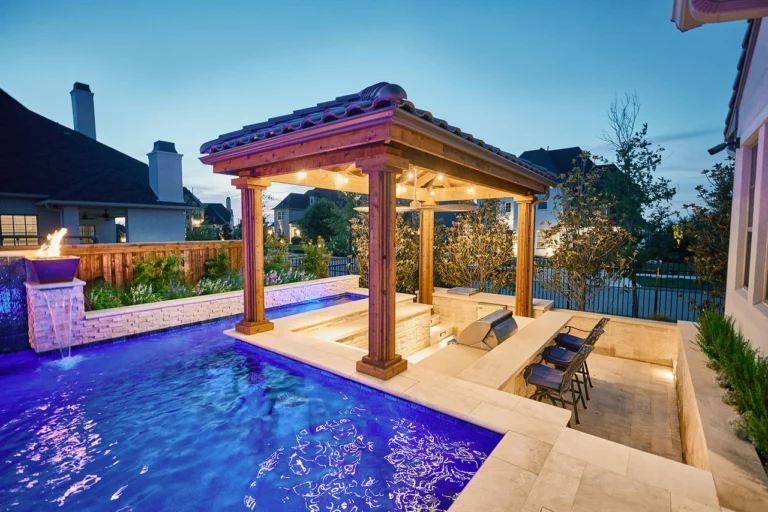 a pergola over an outdoor kitchen next to a pool